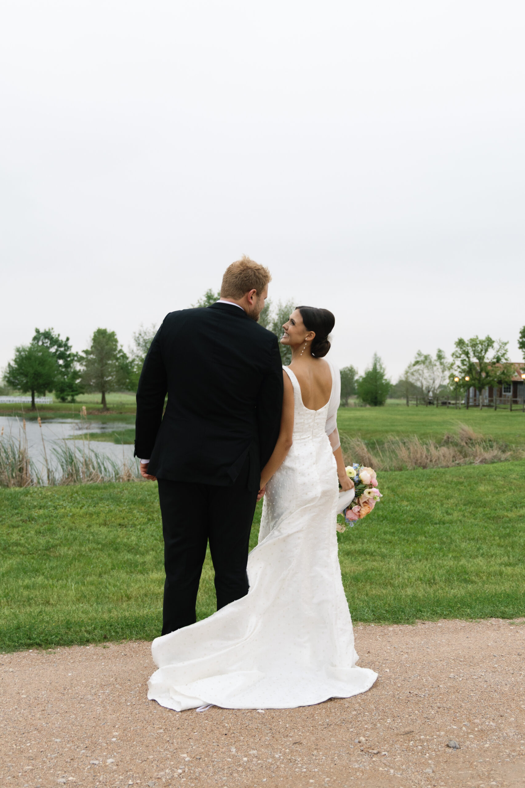 Bride and groom looking at each other holding hands in front of Beckendorff Farms's lake in katy TX