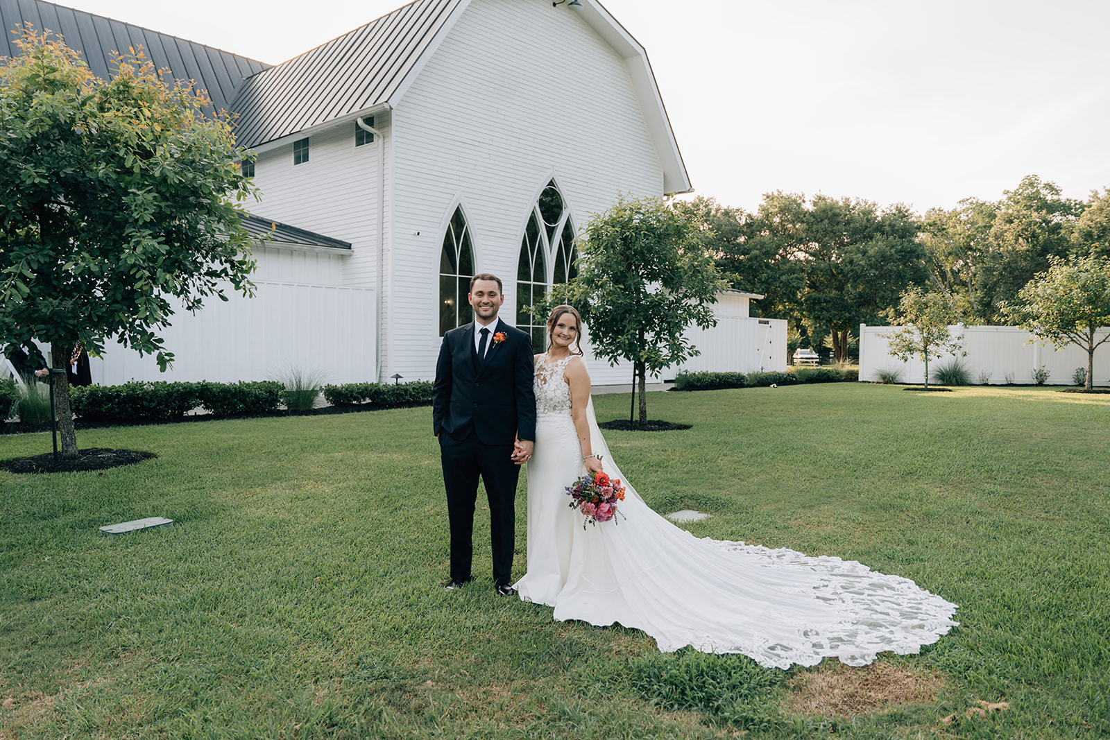 Wide shot of bride and groom holding hands with rustic barn backdrop at The Springs Wallisville