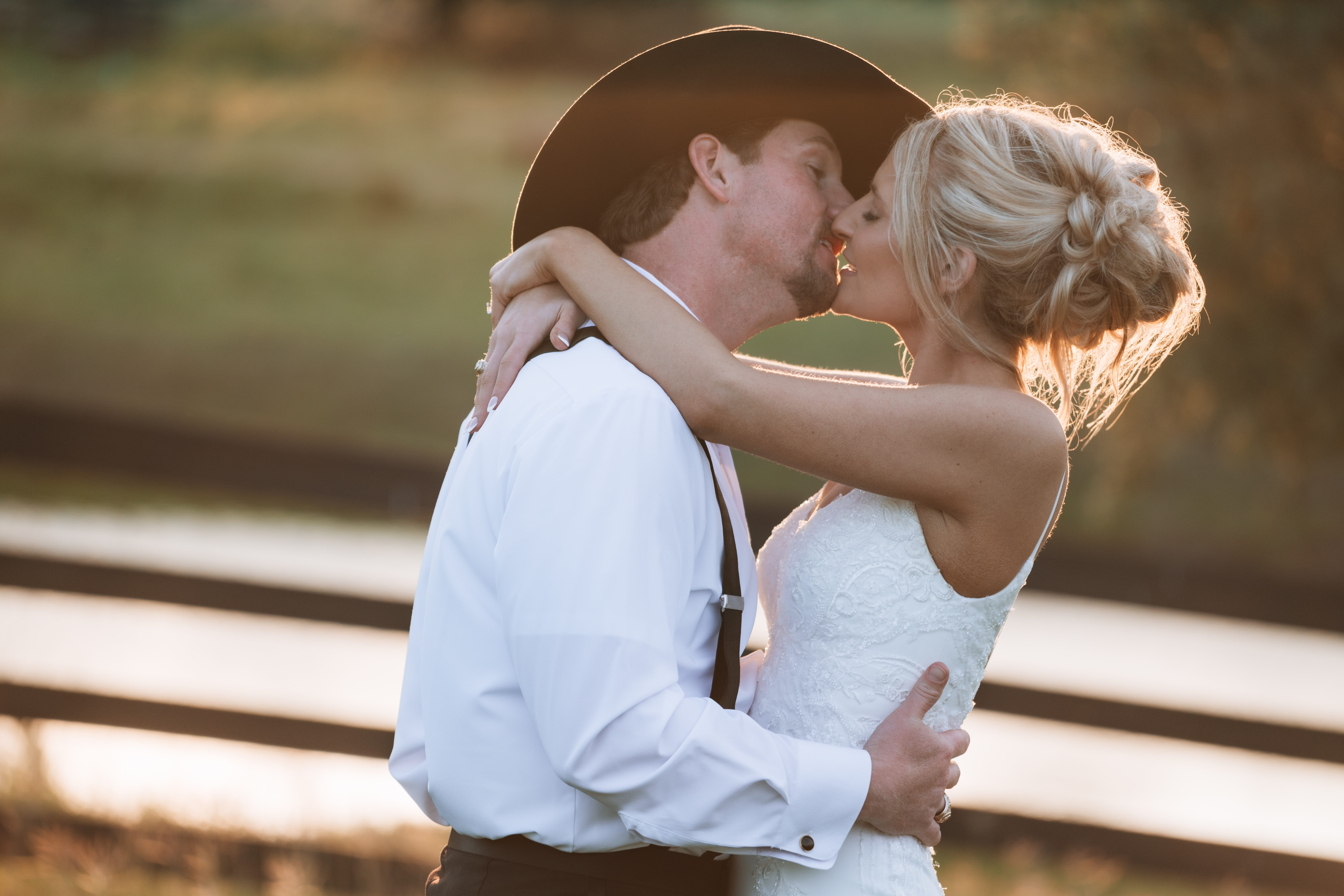 Intimate golden hour kiss at The Oaks at High Hill ranch wedding with a cowboy hat.
